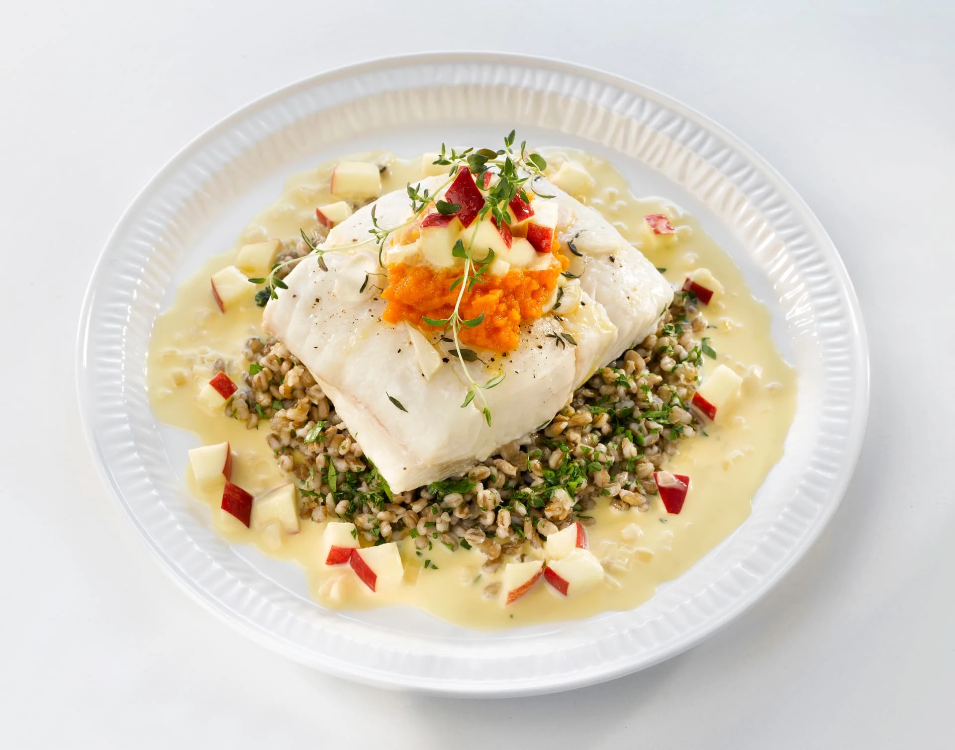 Portion de poisson blanc cuite, servie avec des céréales, des légumes et une sauce