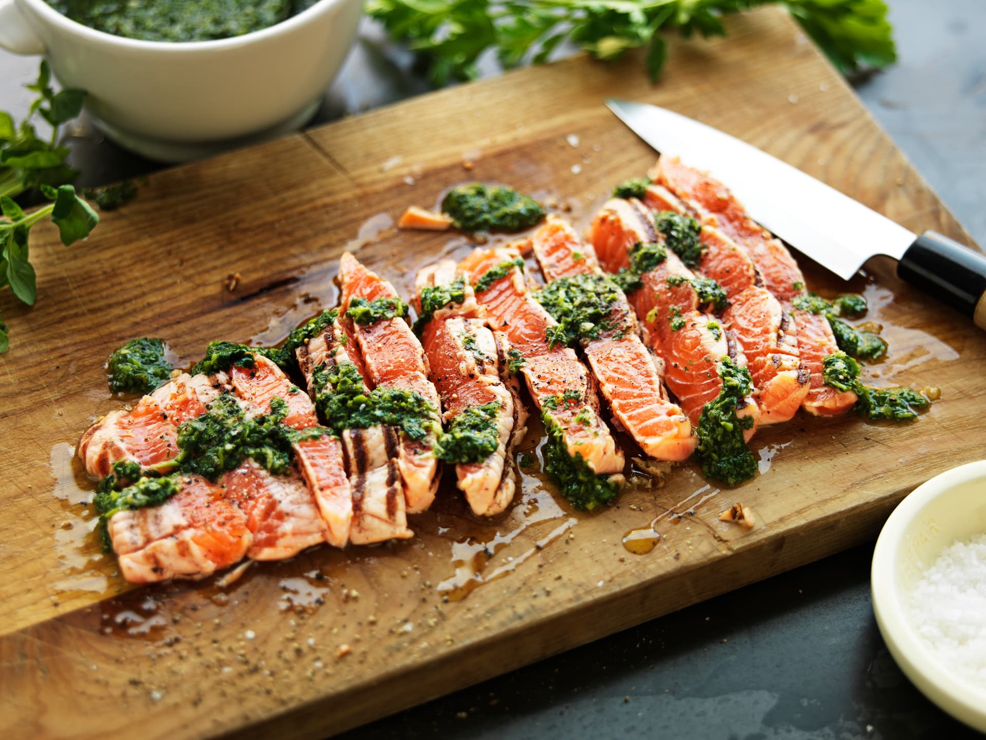Cooked salmon portions served with green herb sauce on a wooden board